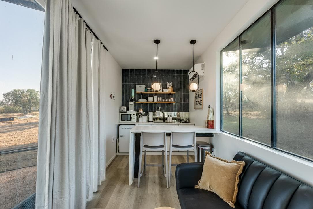 Family Haven open kitchen and living area with a black leather sofa and full-length windows looking out to the ranch