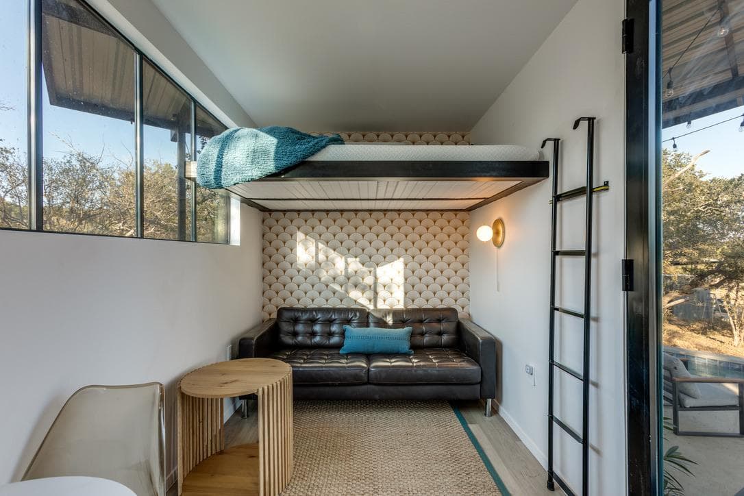 Sunset Loft elevated sleeping loft reached by a ladder, above a black leather sofa